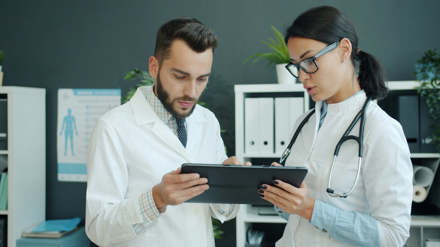 Zwei Ärzte, die in einer Klinik an einem digitalen Tablet zusammenarbeiten.