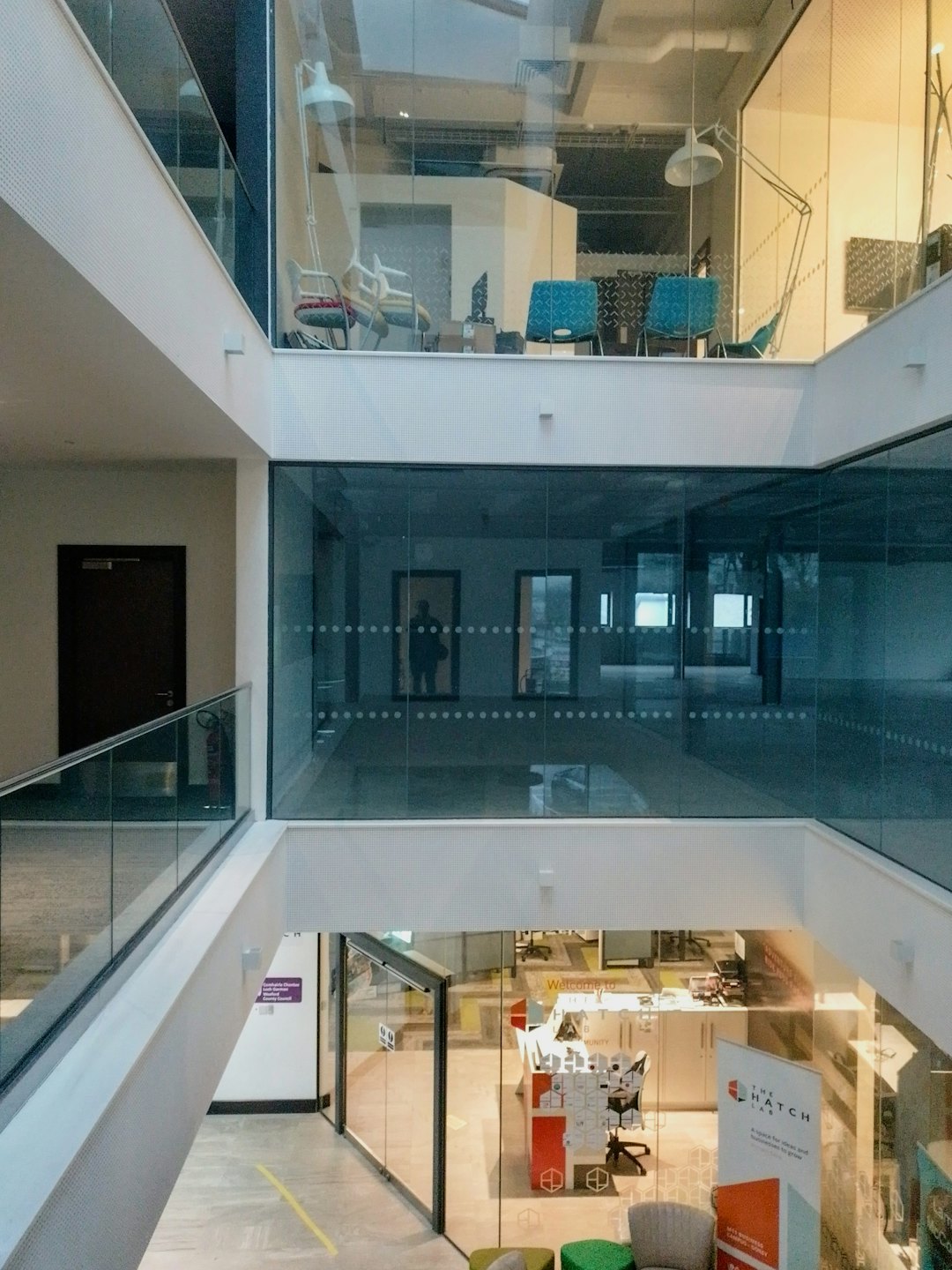 Modernes Bürogebäude-Atrium mit Glaswänden und bunten Stühlen.